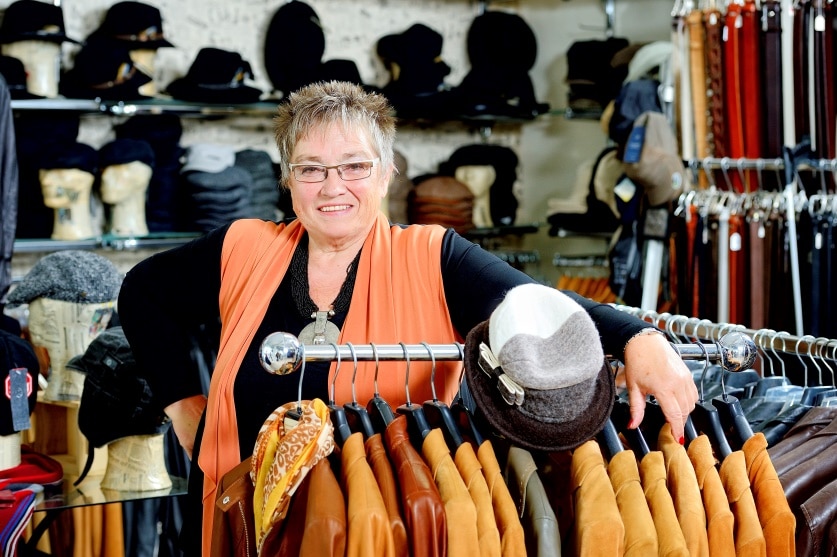 Eine lächelnde Ingrid Schrey hinter einem fahrbaren Ständer mit vielen braunen Lederjacken
