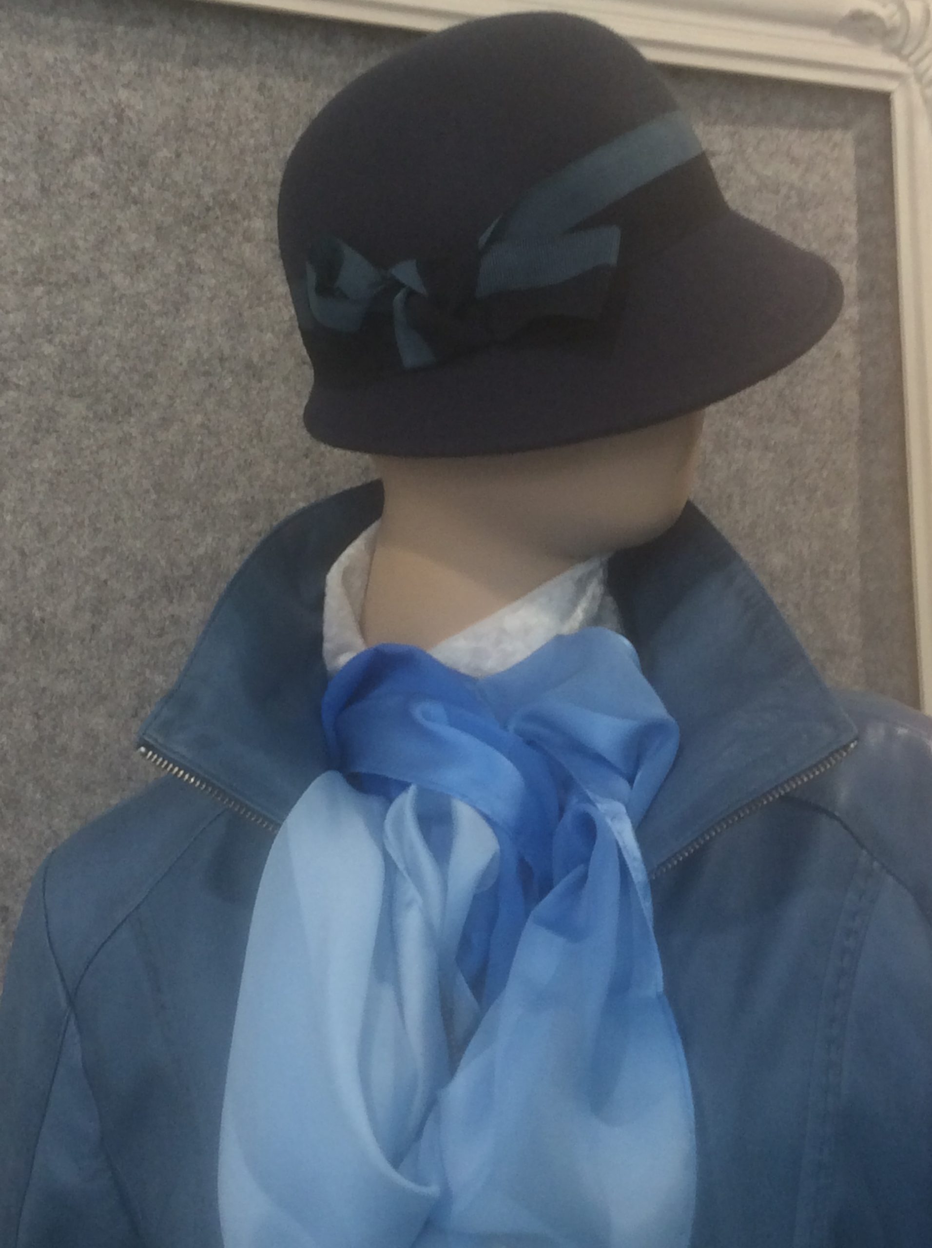 Ein schwarzer Damenhut mit einer blauen Lederjacke und blauem Schal