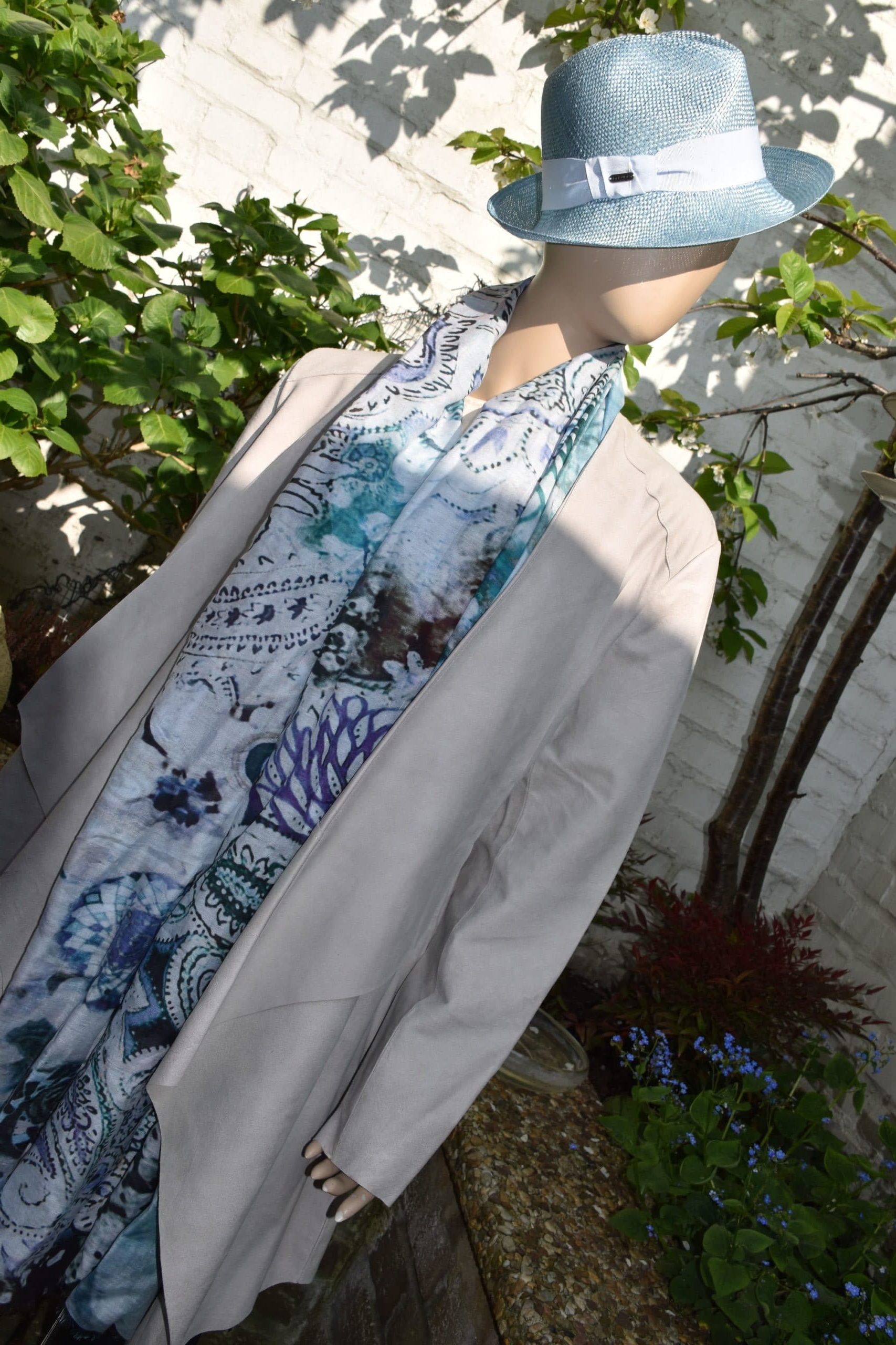 Ein Cremé farbener Kurzmantel für die Frau mit einem langen Schal in Grün- und Blautönen